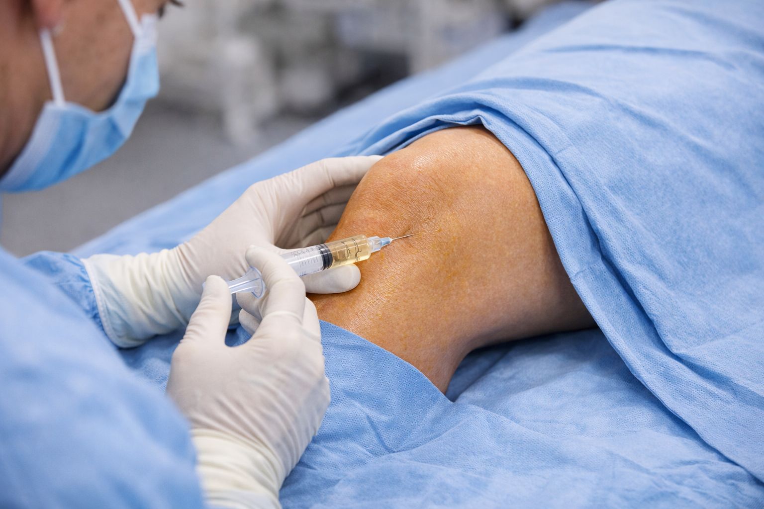 Ein Arzt infiltriert das Kniegelenk eines Patienten mit einer Spritze